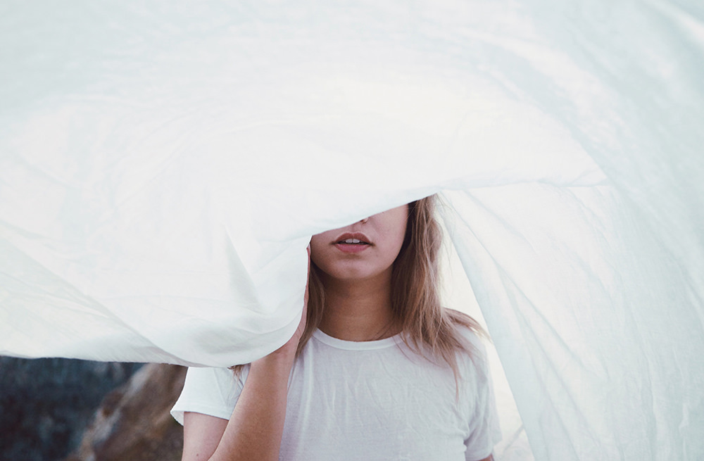 Lonely girl with white sheet covering face